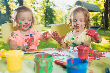 Image showing Two-year old girls painting with poster paintings together against green lawn