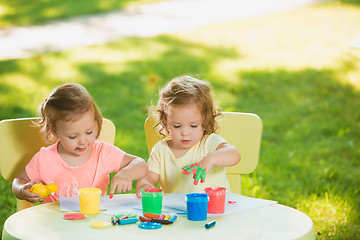 Image showing Two-year old girls painting with poster paintings together against green lawn