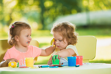 Image showing Two-year old girls painting with poster paintings together against green lawn