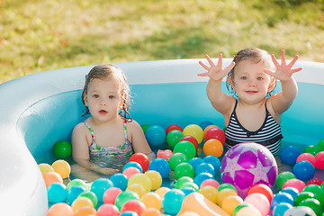 Image showing The two little baby girls playing with toys in inflatable pool in the summer sunny day