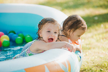 Image showing The two little baby girls playing with toys in inflatable pool in the summer sunny day