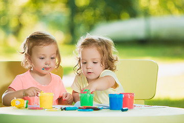 Image showing Two-year old girls painting with poster paintings together against green lawn