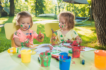 Image showing Two-year old girls painting with poster paintings together against green lawn