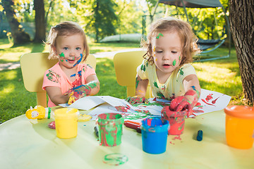 Image showing Two-year old girls painting with poster paintings together against green lawn