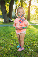 Image showing Two-year old girl stained in colors against green lawn