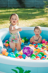 Image showing The two little baby girls playing with toys in inflatable pool in the summer sunny day