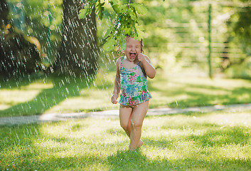 Image showing The little baby girl playing with garden sprinkler.