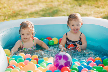 Image showing The two little baby girls playing with toys in inflatable pool in the summer sunny day