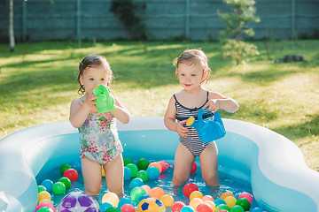 Image showing The two little baby girls playing with toys in inflatable pool in the summer sunny day