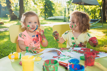 Image showing Two-year old girls painting with poster paintings together against green lawn