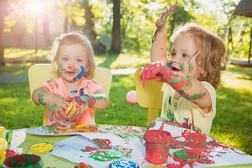 Image showing Two-year old girls painting with poster paintings together against green lawn