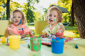 Image showing Two-year old girls painting with poster paintings together against green lawn