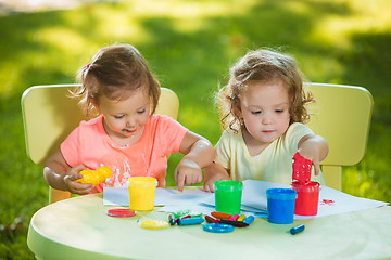 Image showing Two-year old girls painting with poster paintings together against green lawn