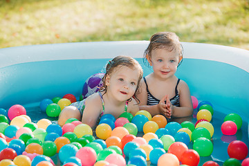 Image showing The two little baby girls playing with toys in inflatable pool in the summer sunny day