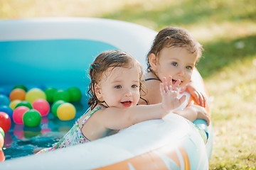 Image showing The two little baby girls playing with toys in inflatable pool in the summer sunny day