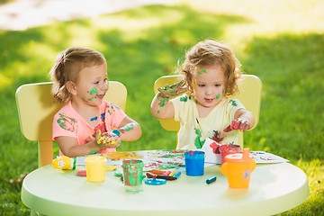 Image showing Two-year old girls painting with poster paintings together against green lawn