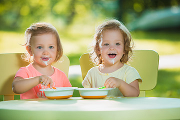 Image showing Two little girls sitting at a table and eating together against green lawn