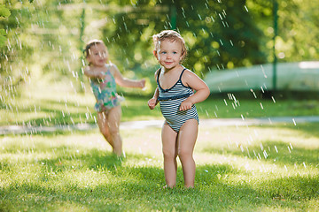 Image showing The two little baby girls playing with garden sprinkler.