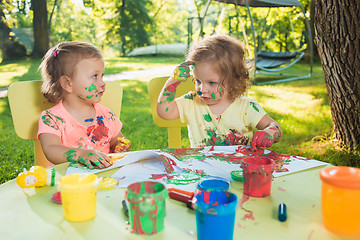 Image showing Two-year old girls painting with poster paintings together against green lawn