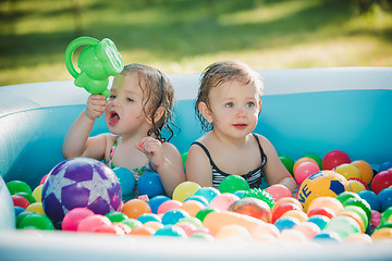 Image showing The two little baby girls playing with toys in inflatable pool in the summer sunny day