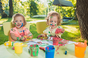 Image showing Two-year old girls painting with poster paintings together against green lawn