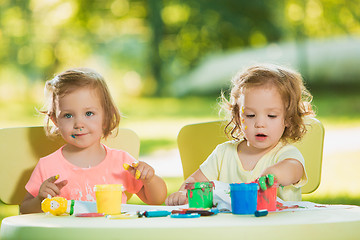 Image showing Two-year old girls painting with poster paintings together against green lawn