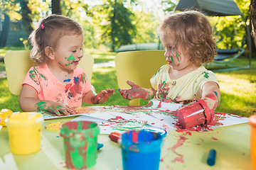 Image showing Two-year old girls painting with poster paintings together against green lawn