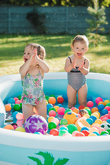 Image showing The two little baby girls playing with toys in inflatable pool in the summer sunny day