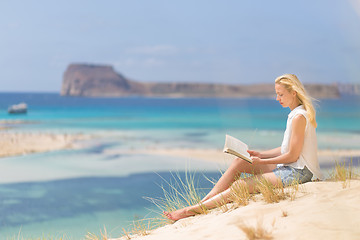 Image showing Woman reading book, enjoying sun on beach.