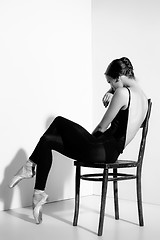 Image showing Ballerina in black outfit posing on a wooden chair, studio background.