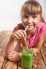 Image showing Girl lying on wooden floor and drinking green smoothie