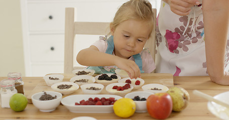 Image showing Little girl placing berries on muffins