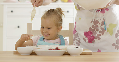 Image showing Laughing girl with muffin cups and parent in apron