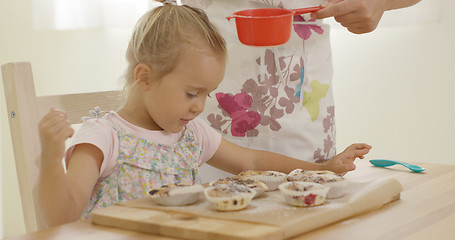 Image showing Child interested in sugar falling on baked muffins