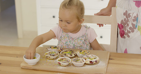 Image showing Close up on girl sprinkling toppings  muffins