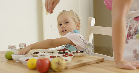 Image showing Child watching woman sprinkle candy on muffins