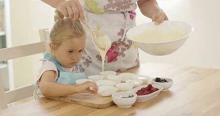 Image showing Parent pouring muffin batter into holders