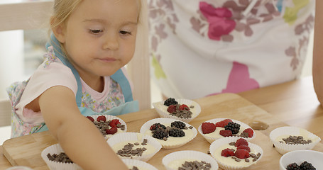 Image showing Cute little girl putting berries on muffins