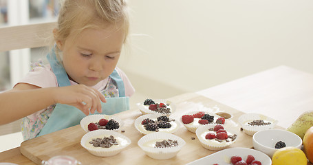 Image showing Girl putting berries on muffins  table