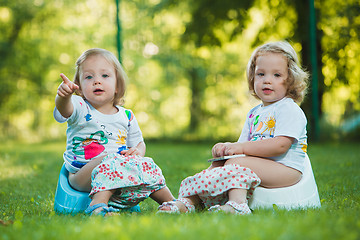 Image showing The two little baby girls sitting on pottys against green grass