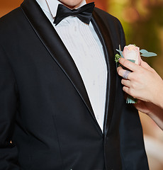 Image showing Bride arranging boutonniere flower on suit jacke groom