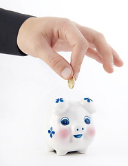 Image showing Hand inserting coin into piggy-bank