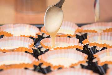 Image showing The dough for cakes dripping from a spoon into molds