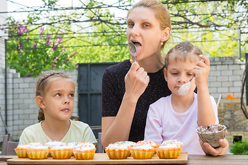 Image showing Mother and two daughters lick spoons with confectionery icing for Easter cupcakes