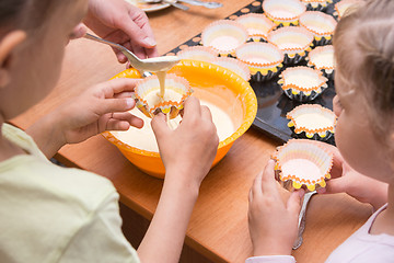 Image showing Two girls helped mom to pour batter into the molds for cupcakes