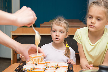 Image showing Two girls with a surprised look like mom pours batter into molds for cupcakes