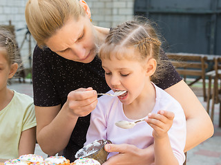 Image showing Mother feeding daughter with spoon confectionery glaze for cooking cakes
