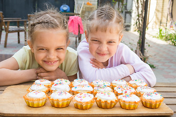 Image showing Two girls pretending funny faces, sitting in front of easter cupcakes