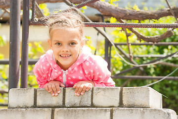 Image showing Seven Years\' happy girl hanging on a brick fence and looked in the frame