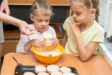 Image showing Mom helps subsidiaries to pour batter into molds for baking cakes